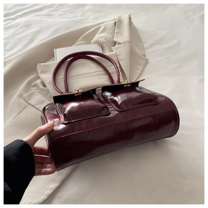 Detail of dark red glossy leather handbag with double front pockets and gold twist locks