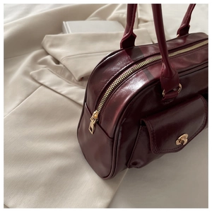 Close-up of glossy deep red leather handbag featuring gold metal turn-lock and handle detail