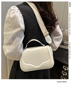 Close-up of stylish white saddle bag with wavy flap design and wide shoulder strap