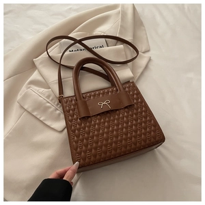 Dettaglio di una borsa trapuntata marrone con fiocco dorato e doppi manici superiori