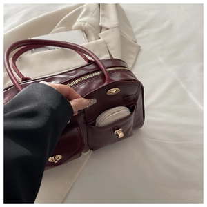 Detail view of burgundy leather handbag showing metallic turn-lock pocket and smooth zipper