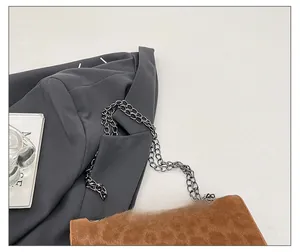 Detail of a brown suede shoulder bag with a thick dark metal chain strap for women