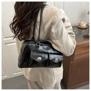 Detail of black glossy underarm bag featuring dual flap pockets and gold hardware