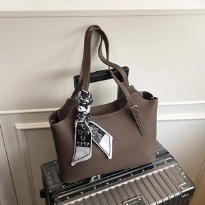 Brown leather tote bag with silk scarf on metallic suitcase for travel