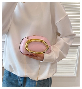 Detail of light pink crossbody bag featuring a large oval gold handle and chain strap