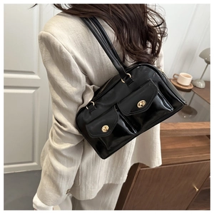 Detail of glossy black underarm bag with gold twist locks on white suit jacket
