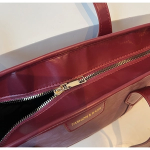 Detail of burgundy tote bag showing top zipper and gold Fashion & Bags logo lettering