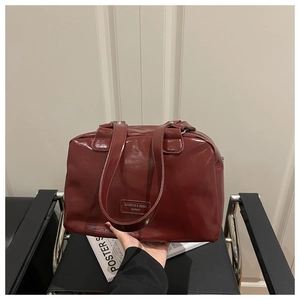 Detail view of the deep red oil-wax leather handbag with fashion logo patch on a black chair
