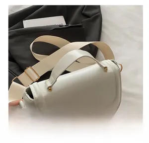 Detail view of white crossbody bag with thick woven strap and gold metal buckles