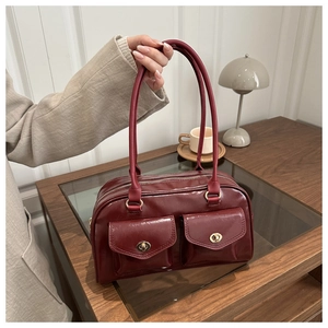 Macro detail of wine red glossy handbag featuring double front pockets and gold twist locks