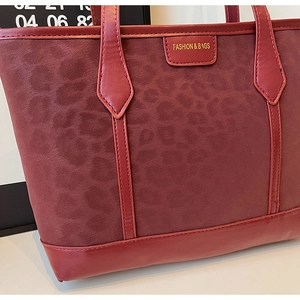 Macro shot of dark red leopard print suede texture and gold fashion logo on tote bag