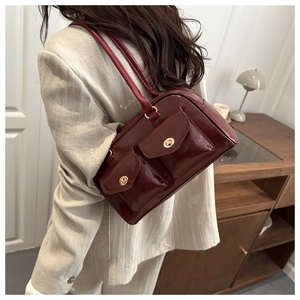 Close-up of a burgundy patent leather square handbag with golden hardware on a model