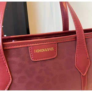 Close-up of wine red suede tote bag detail featuring a leather label and gold logo text