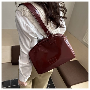 Close-up of a burgundy glossy leather tote bag worn as a shoulder bag on model