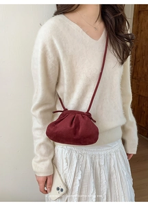 Dettaglio di una borsa a tracolla plissettata bordeaux indossata da una modella sobria