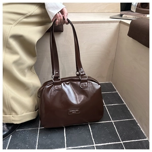 Close-up of a glossy dark brown leather handbag featuring silver rings and brand tag