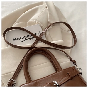 Detail of brown vintage shoulder bag with faux leather texture and buckle element