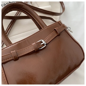 Detailed close-up of brown glossy oil leather handbag with decorative buckle and fine stitching