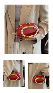 Detail of red oval leather handbag featuring a gold metal handle and slim chain strap