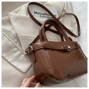 Detailed view of brown retro glossy faux leather handbag with metal buckle on a blazer