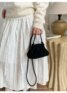 Dettaglio di una borsa a nuvola plissettata nera tenuta da una modella in ambiente accogliente