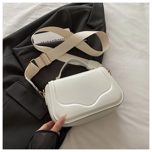 Detail of white textured flap bag with wavy pattern and wide fabric strap on a blazer