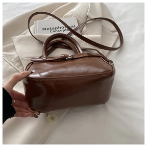 Chic brown glossy leather handbag with silver hardware displayed on a cream blazer