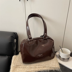 Minimalist dark brown glossy shoulder bag on beige knit fabric in a cozy lifestyle setting