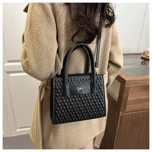 Detail of quilted leather handbag featuring a golden bow metal buckle and sturdy handles
