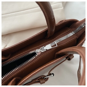 Detail of a brown PU leather handbag featuring a silver metal zipper and fine stitching