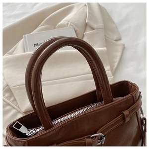 Close-up of a dark brown glossy handbag featuring silver metal zippers and smooth handles