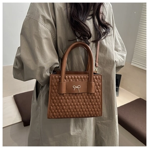 Borsa a tracolla marrone trapuntata con fiocco dorato indossata su abito beige