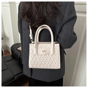 Dettaglio borsa a tracolla trapuntata beige con motivo a rombi e fiocco dorato piccolo