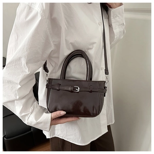 Detail of a shiny dark brown crossbody bag with silver buckle and thin strap on a model