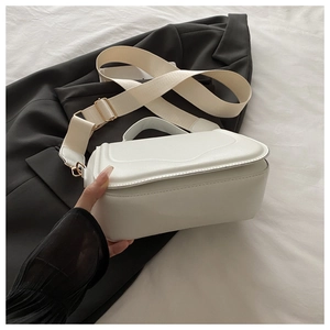 Close-up of white leather crossbody bag with wide fabric strap on a black blazer