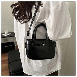 Chic black patent leather crossbody bag styled with white shirt in indoor home setting