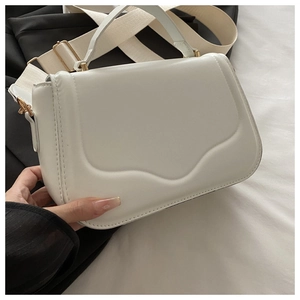 Detail of white leather shoulder bag with wavy flap design and gold hardware accents
