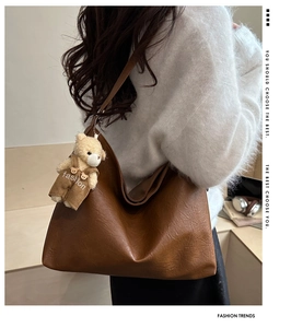 Brown leather tote bag featuring a cute teddy bear charm shown from a side shoulder view