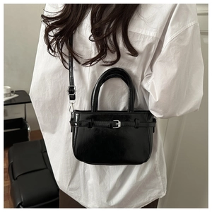 Detail of black patent leather mini bag with decorative buckle and silver hardware strap