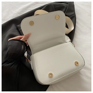 Detail view of white flip-top crossbody bag with gold magnetic buckles and wide strap