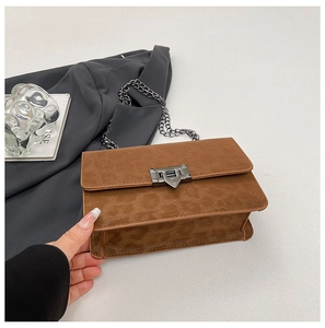 Detail view of brown suede crossbody bag with metallic chain and geometric clasp