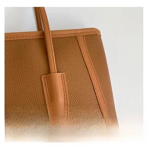 Close-up of litchi grain leather texture and detailed stitching on the brown tote bag