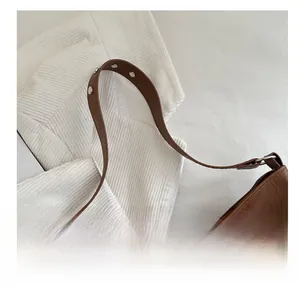 Detail of brown leather shoulder strap featuring silver metal rivets and textured finish