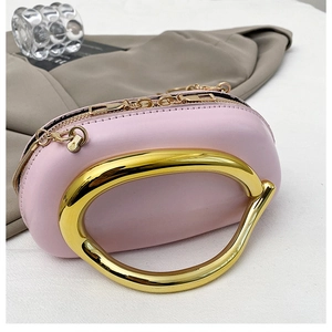 Detail of pink leather handbag with decorative gold C-shaped metal handle and chain strap
