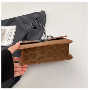 Detail of brown faux suede crossbody bag featuring leopard print base and metal chain