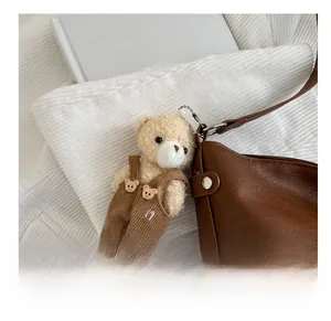 Detail of cute plush bear charm with corduroy overalls hanging on a brown leather bag