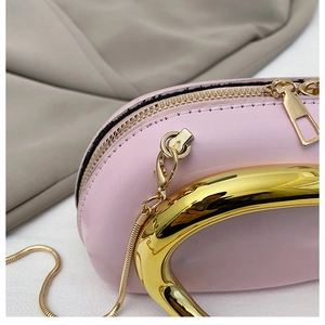 Detail of pink leather handbag featuring a curved gold metal handle and fine stitching