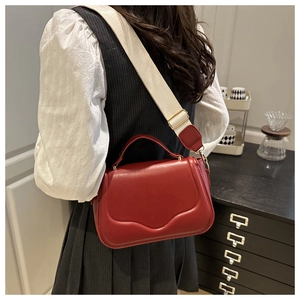 Close-up of red small square bag with white wide fabric strap and golden hardware