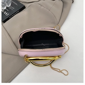 Detail view of pink crossbody bag with gold U-shaped handle and black fabric lining interior