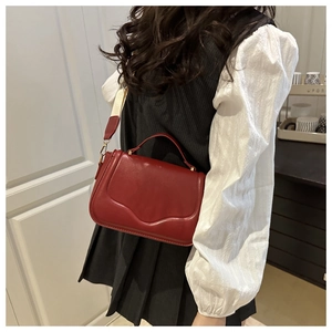 Detail of dark red leather handbag worn by model with textured finish and wide fabric strap
